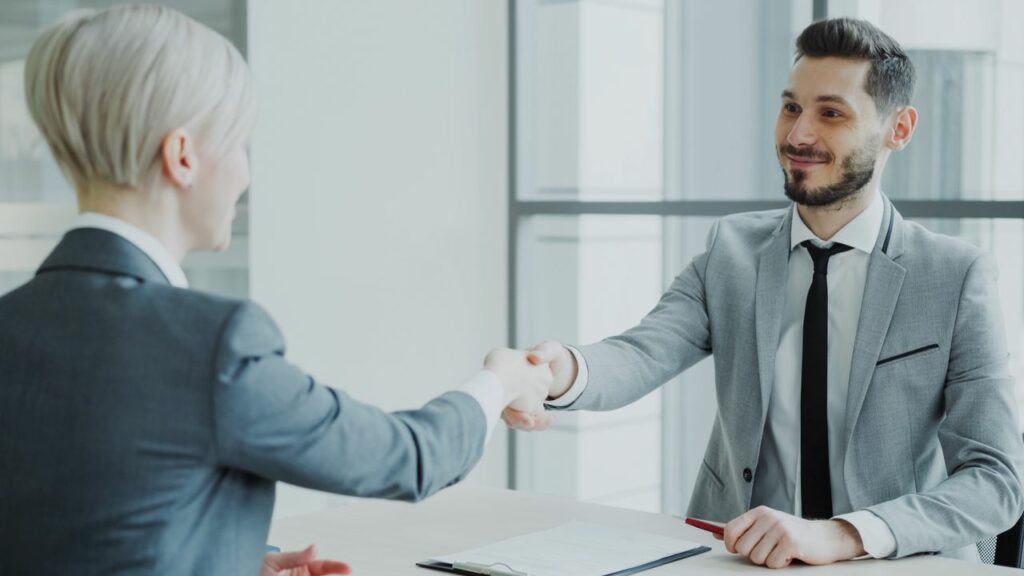 Two professionals shaking hands in a bright, modern office environment.